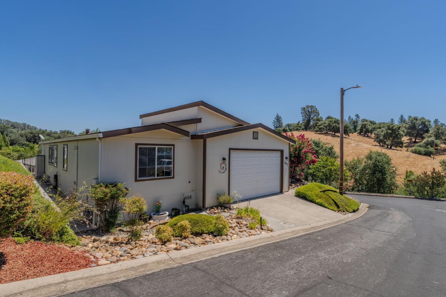Single-story home with a two-car garage, rock garden, and dry hills behind it.