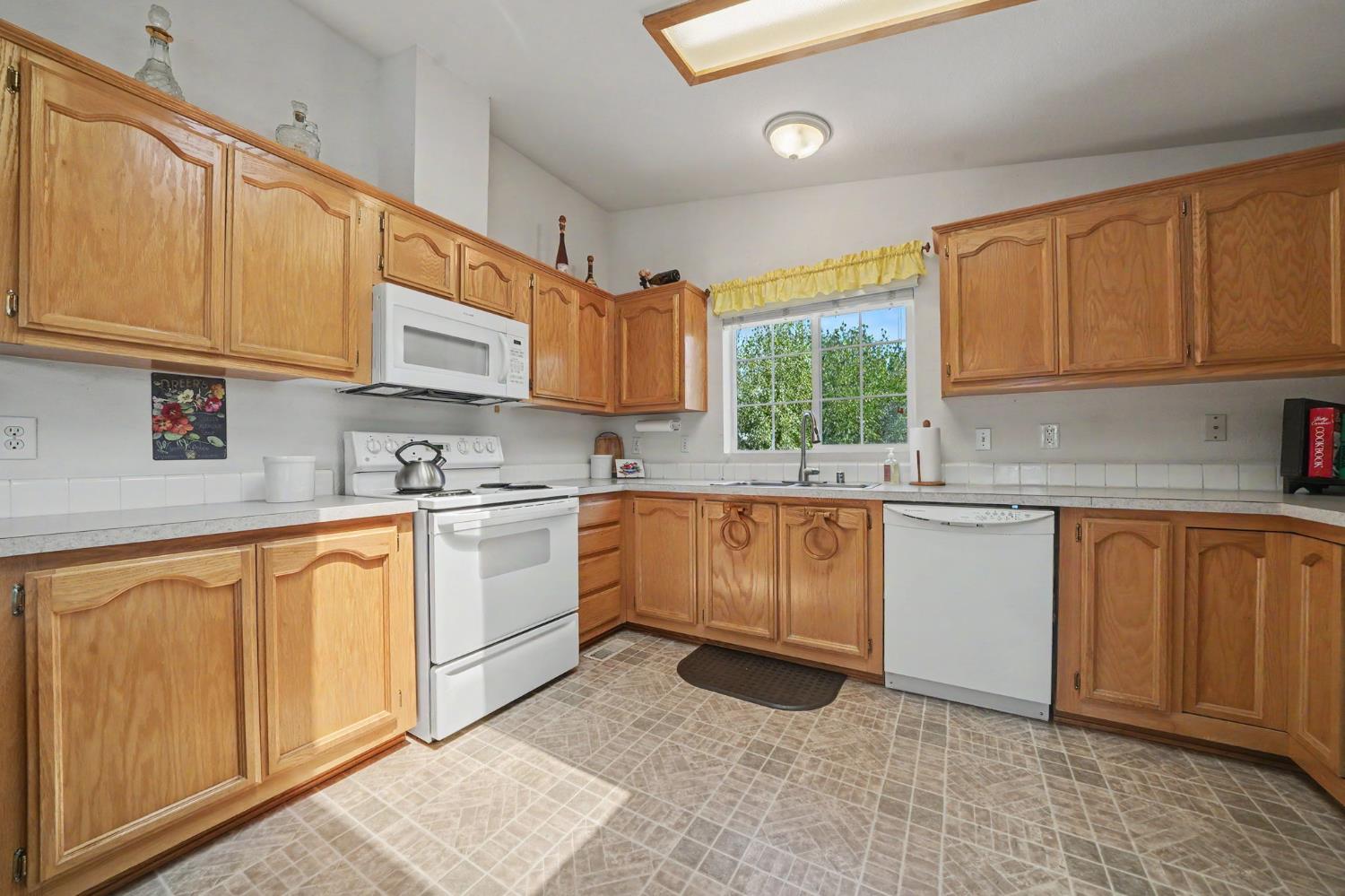 Kitchen with honey-colored cabinets, white appliances, and a window over the sink.