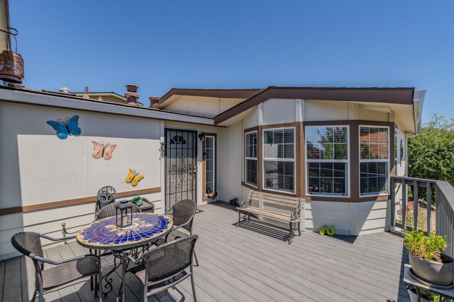 Furnished deck with a mosaic table, wicker chairs, and a bench beside bay windows.
