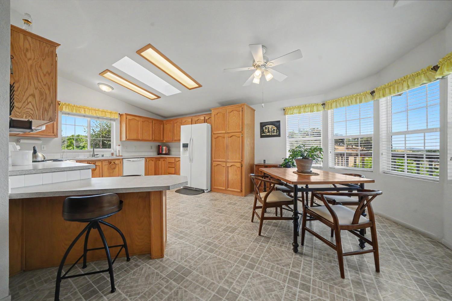 Kitchen and dining area with wood cabinetry, a breakfast peninsula, and a table beside large windows.