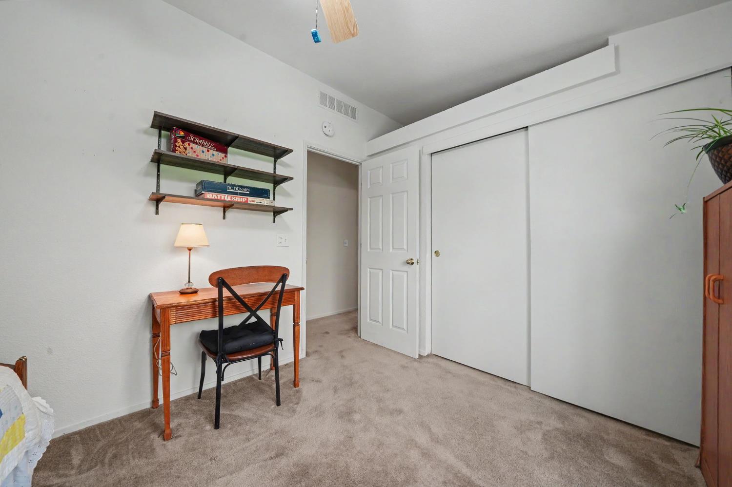 Carpeted bedroom with a desk, wall shelves, and large sliding closet doors.
