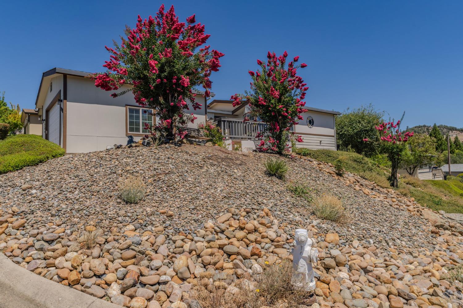 Low, light-colored home on a rocky slope, framed by pink flowering trees.