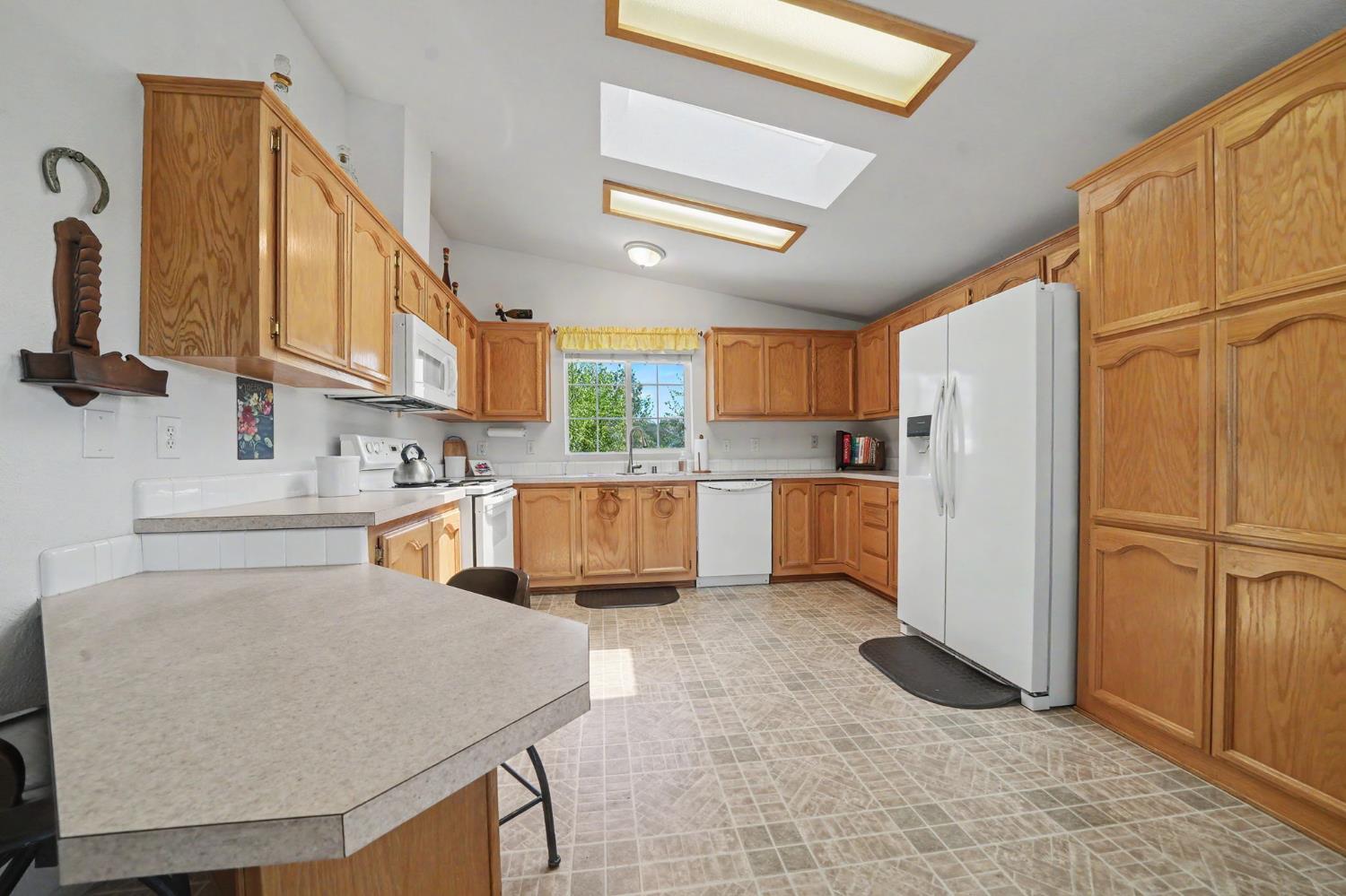 Kitchen with honey-colored wood cabinets, white appliances, and a window above the sink.