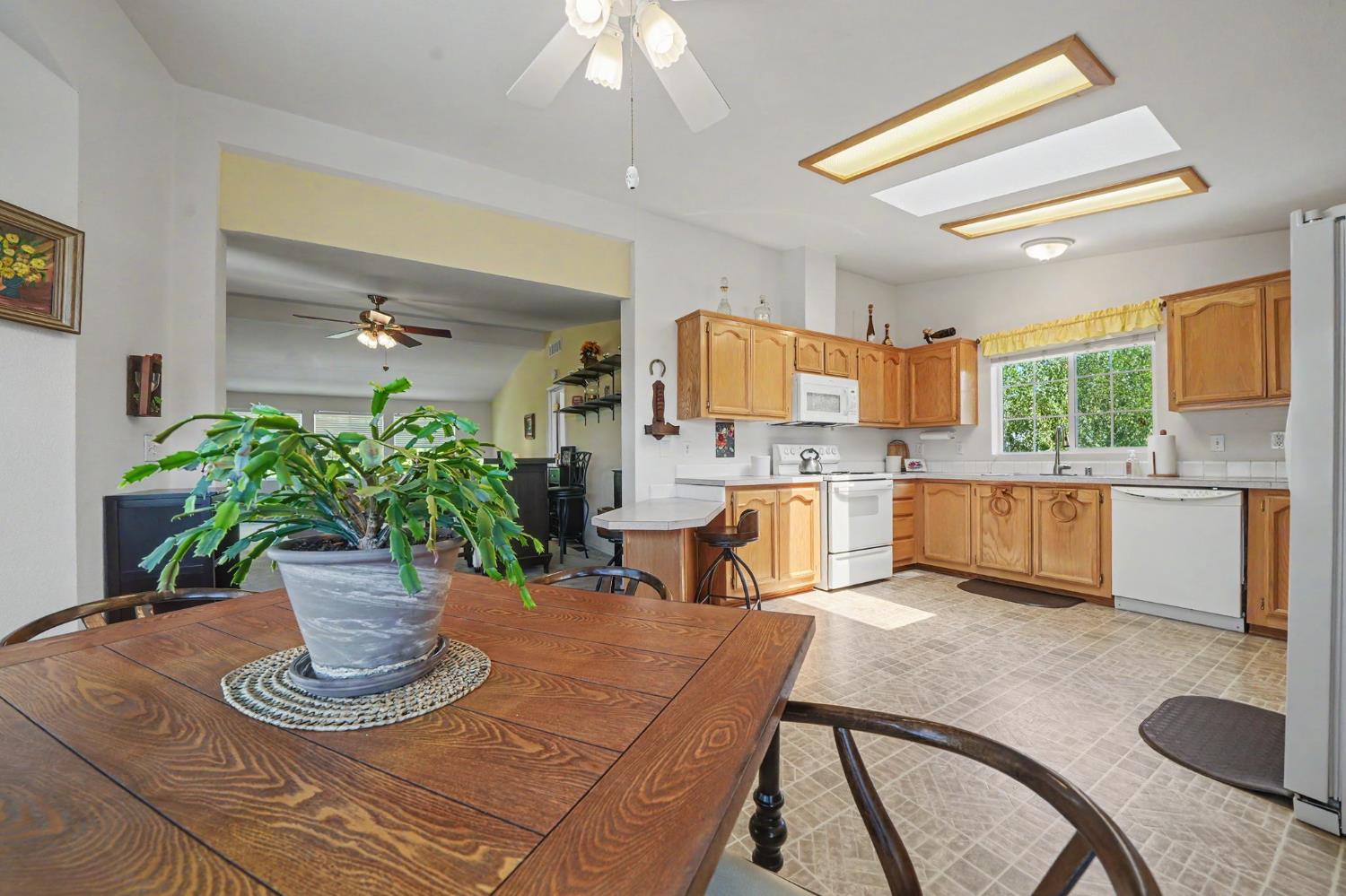Kitchen and dining area with honey-colored cabinets, white appliances, and a large wooden table.
