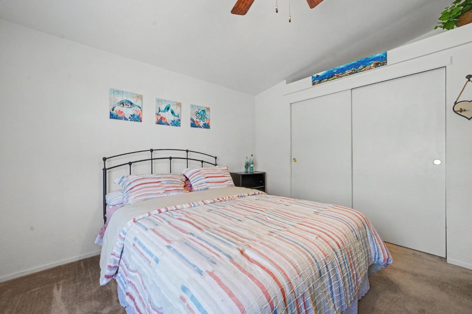 Bedroom with striped bedding, sliding closet doors, and ocean-themed wall art.