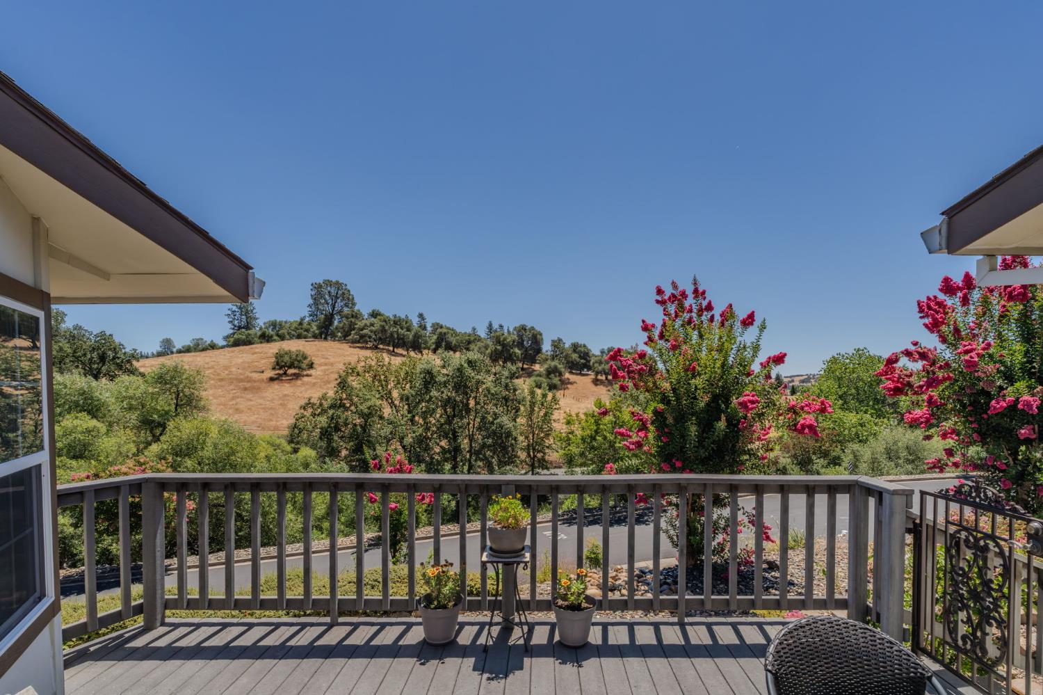 Deck overlooking flowering trees and dry, tree-dotted hills.