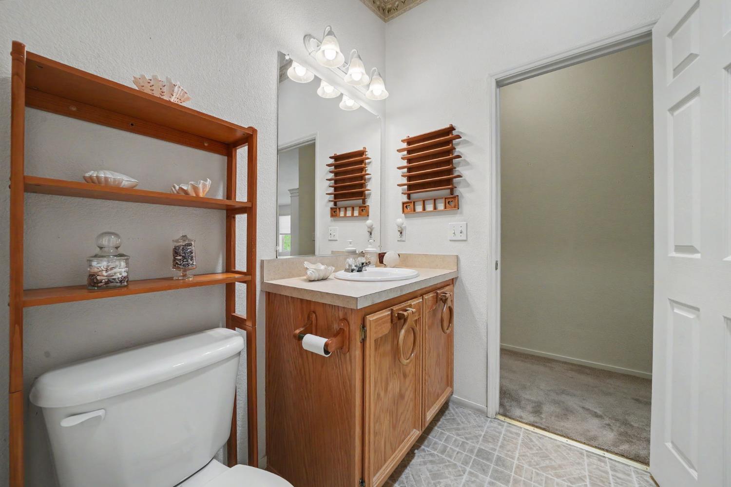 Bathroom with a wood vanity, large mirror, and open shelving beside the toilet.