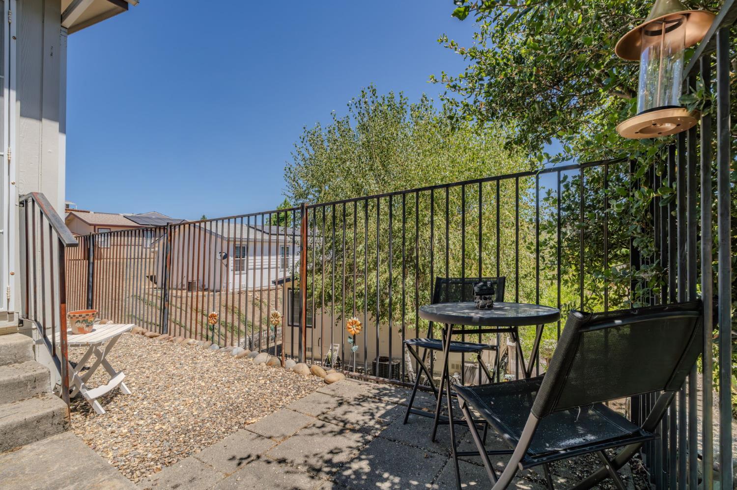 Patio with black railings, outdoor table and chairs, lounge seating, and leafy trees.