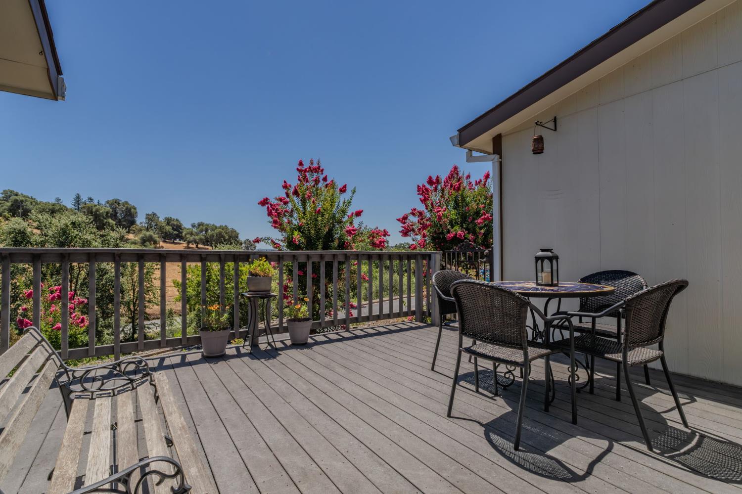 Furnished wooden deck with outdoor dining set overlooking flowering trees and a wooded hillside.