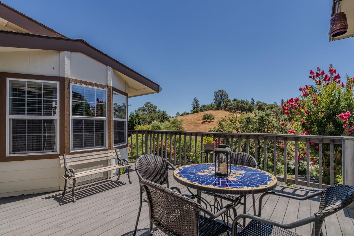 Deck with a blue tiled table and seating, overlooking flowering shrubs and rolling hills.