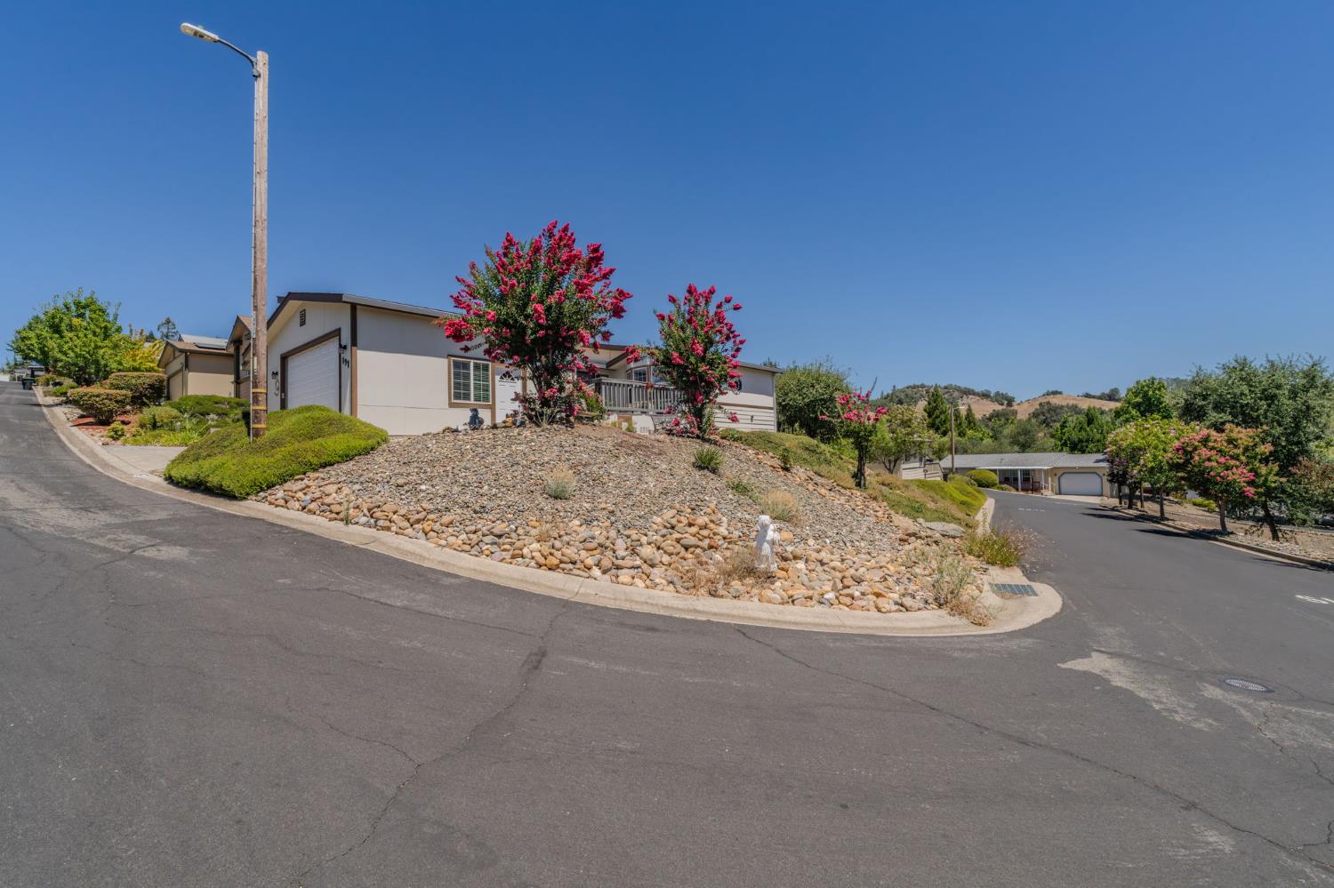 Single-story home on a landscaped corner lot with a rock garden and pink flowering trees.
