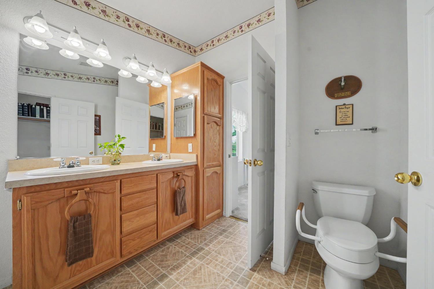 Bathroom with a double-sink wood vanity, large mirror, and separate toilet area.