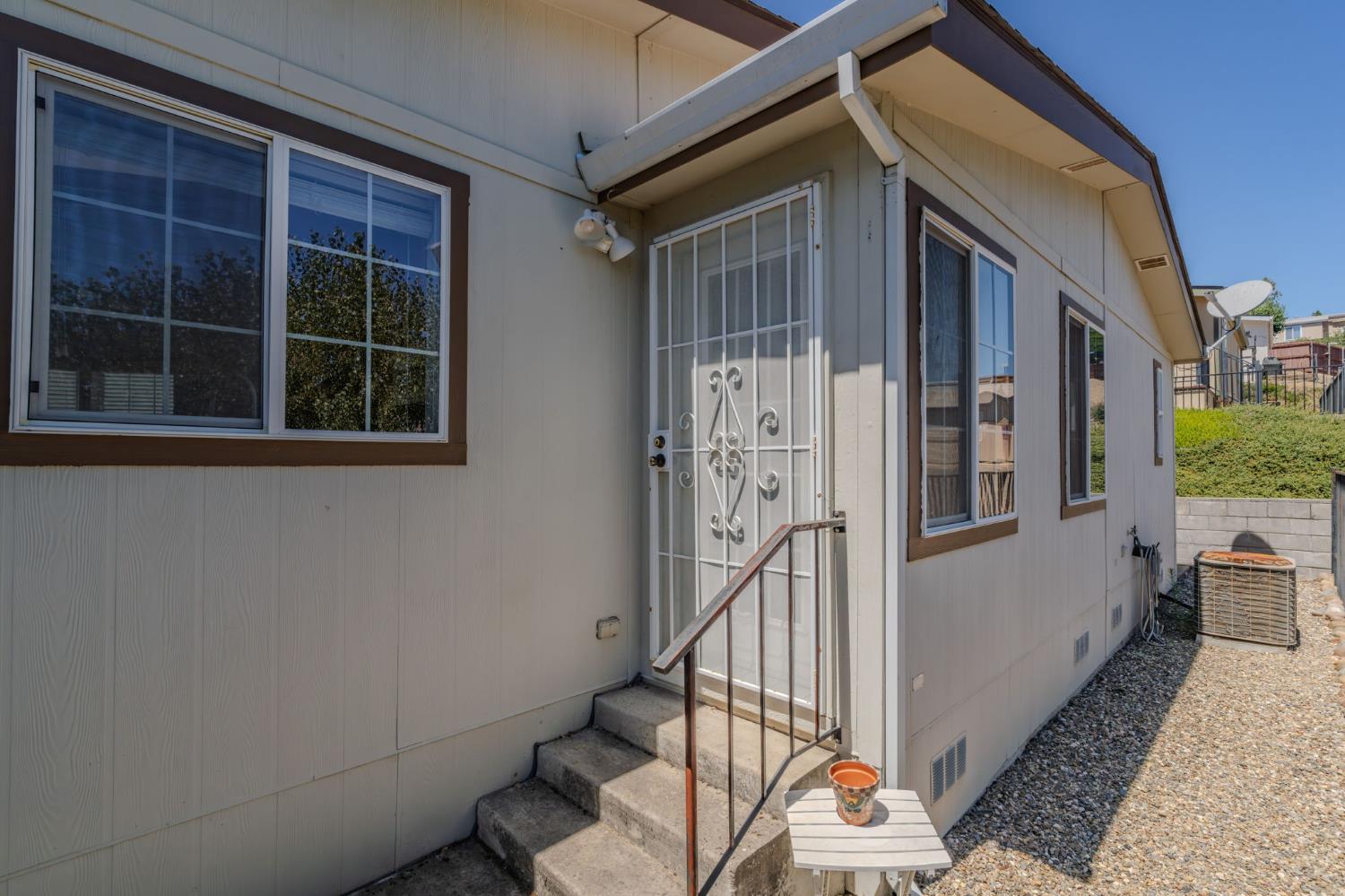 Home exterior with barred entry door, concrete steps, and gravel side yard.