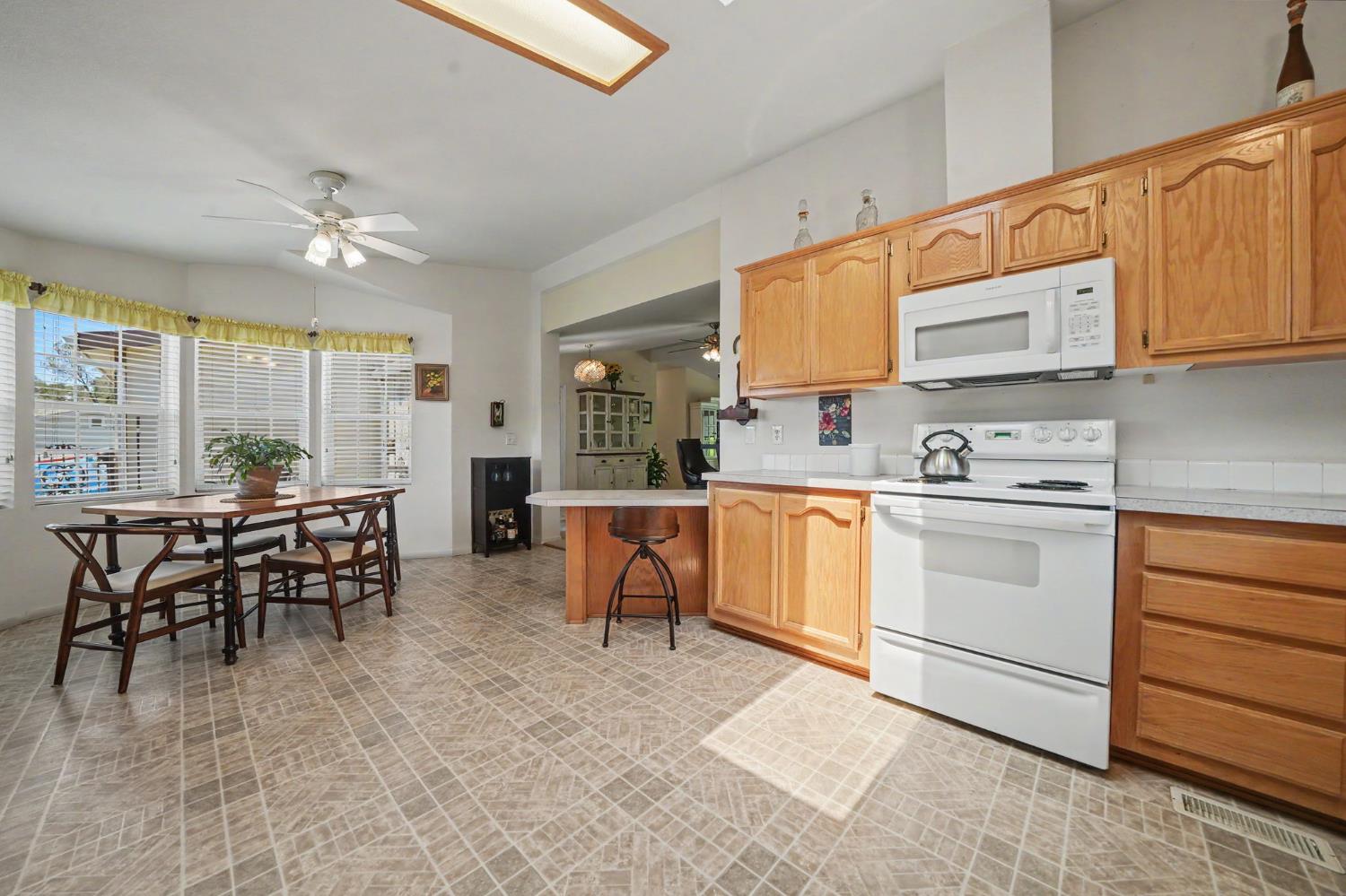 Kitchen with wood cabinets and white appliances, adjoining a dining area beside wide windows.