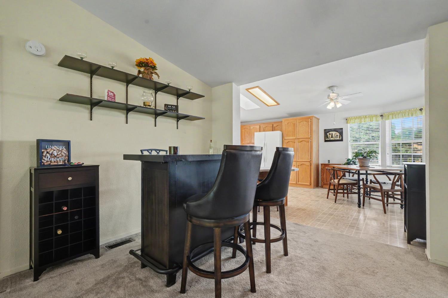 Open-plan kitchen and dining area with a dark breakfast bar, tall stools, and honey-colored cabinets.