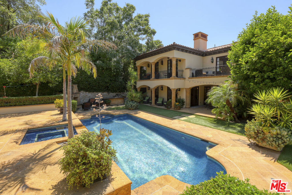 Backyard pool and raised spa beside a Mediterranean-style home with a balcony and palm trees.