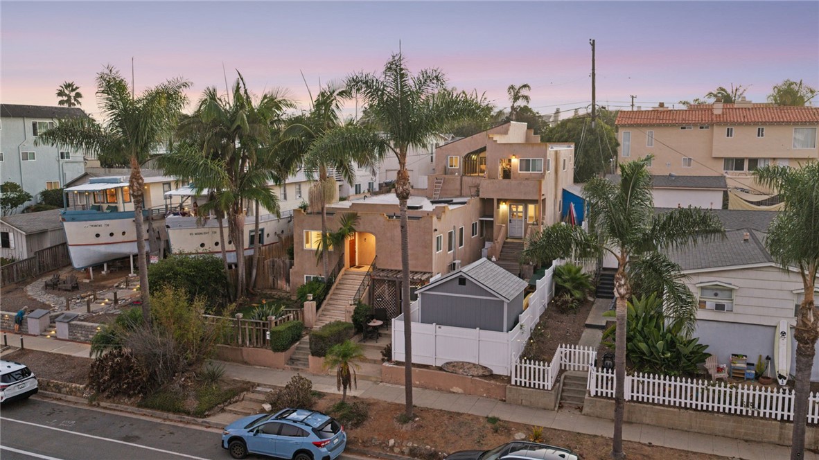 Residential homes with palm trees and fenced yards along a street at dusk.