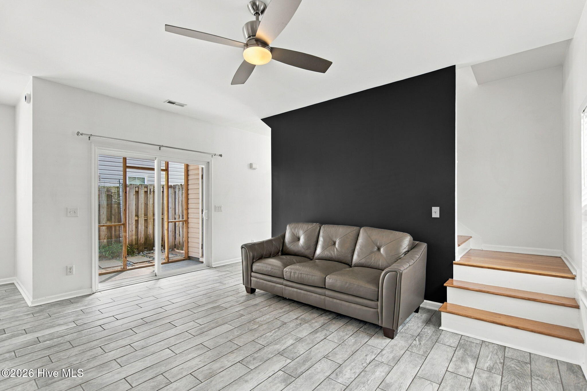 Living room with a gray leather sofa, dark accent wall, sliding glass doors, and wood-tread steps.