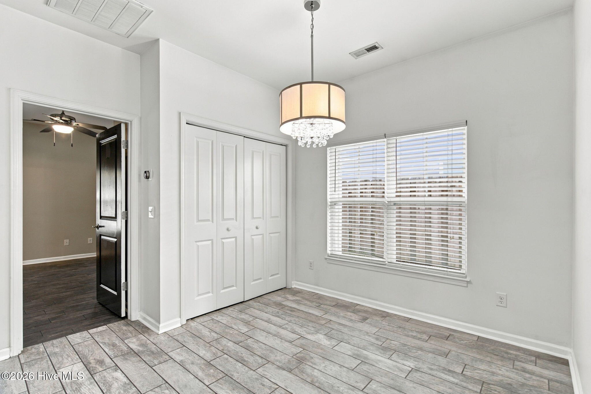 Empty room with gray wood-look tile, white closet doors, a window with blinds, and a chandelier.