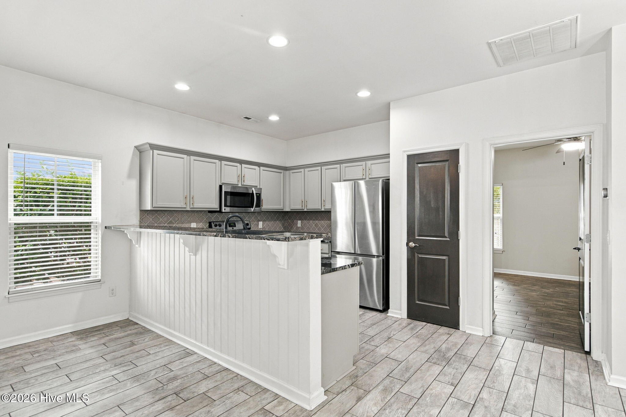 Vacant kitchen with gray cabinetry, stainless appliances, and a breakfast bar with dark stone countertop.