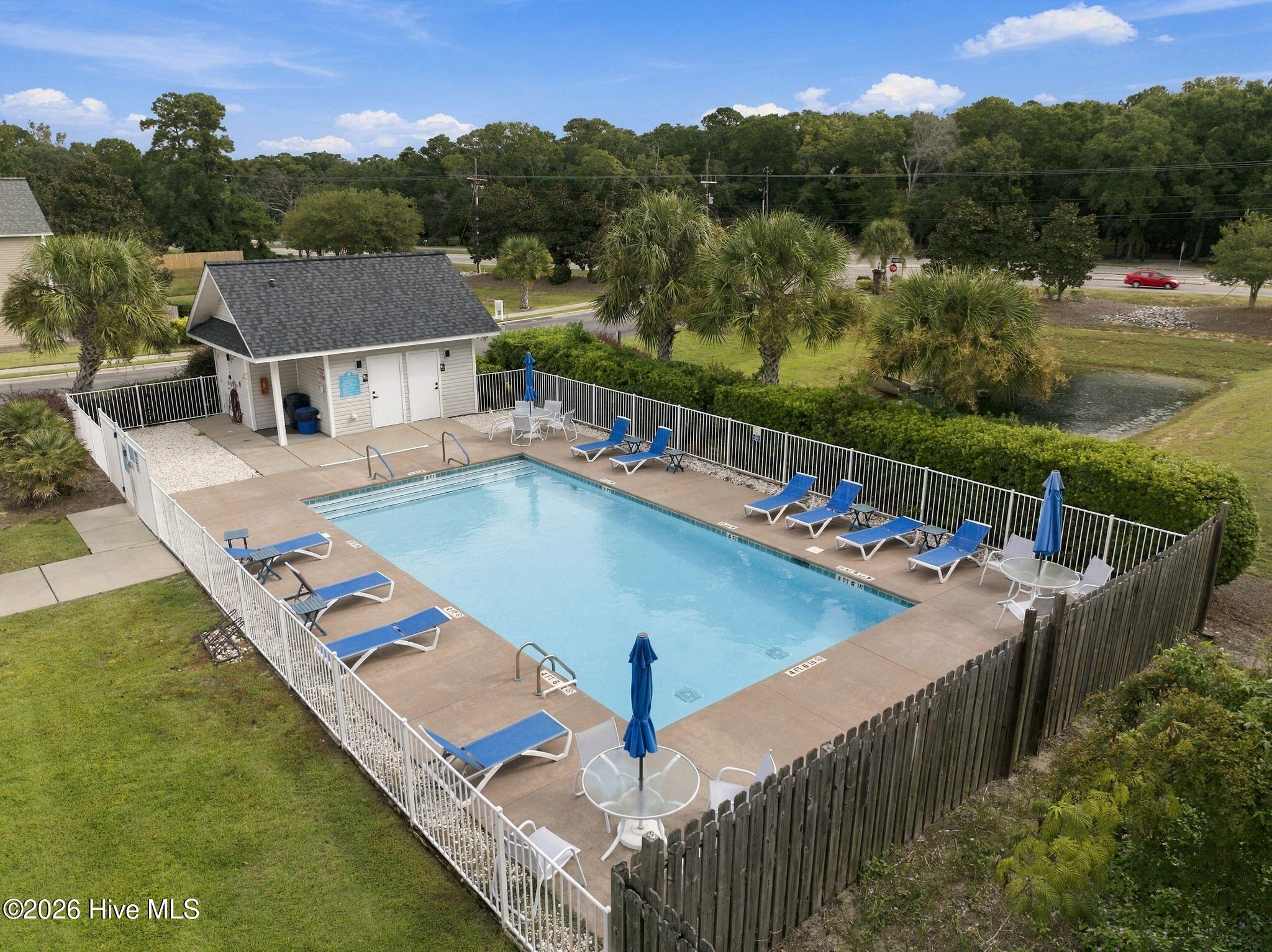Outdoor swimming pool with blue lounge chairs, umbrellas, and a fenced patio.
