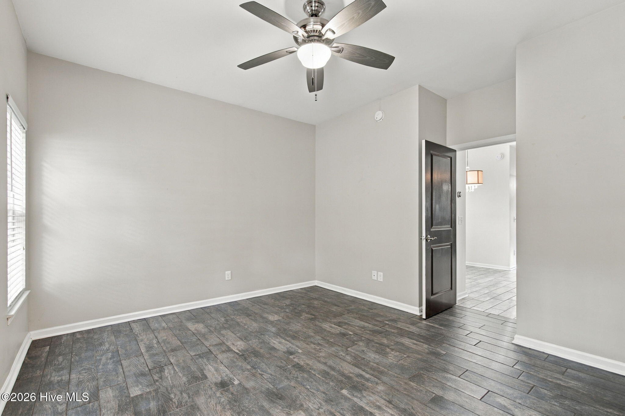 Empty room with gray-brown plank flooring, a ceiling fan, and an open doorway to a tiled area.