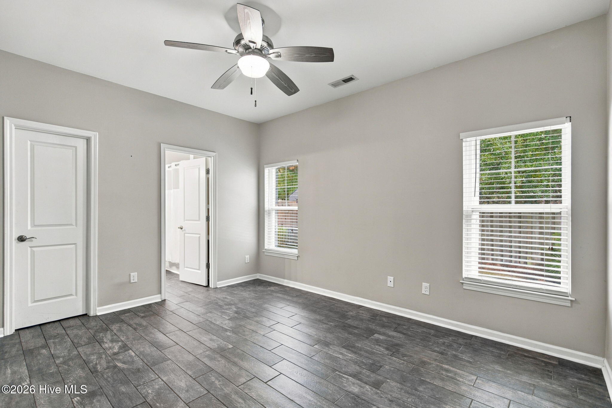 Empty bedroom with gray tile flooring, two blinded windows, and a ceiling fan.