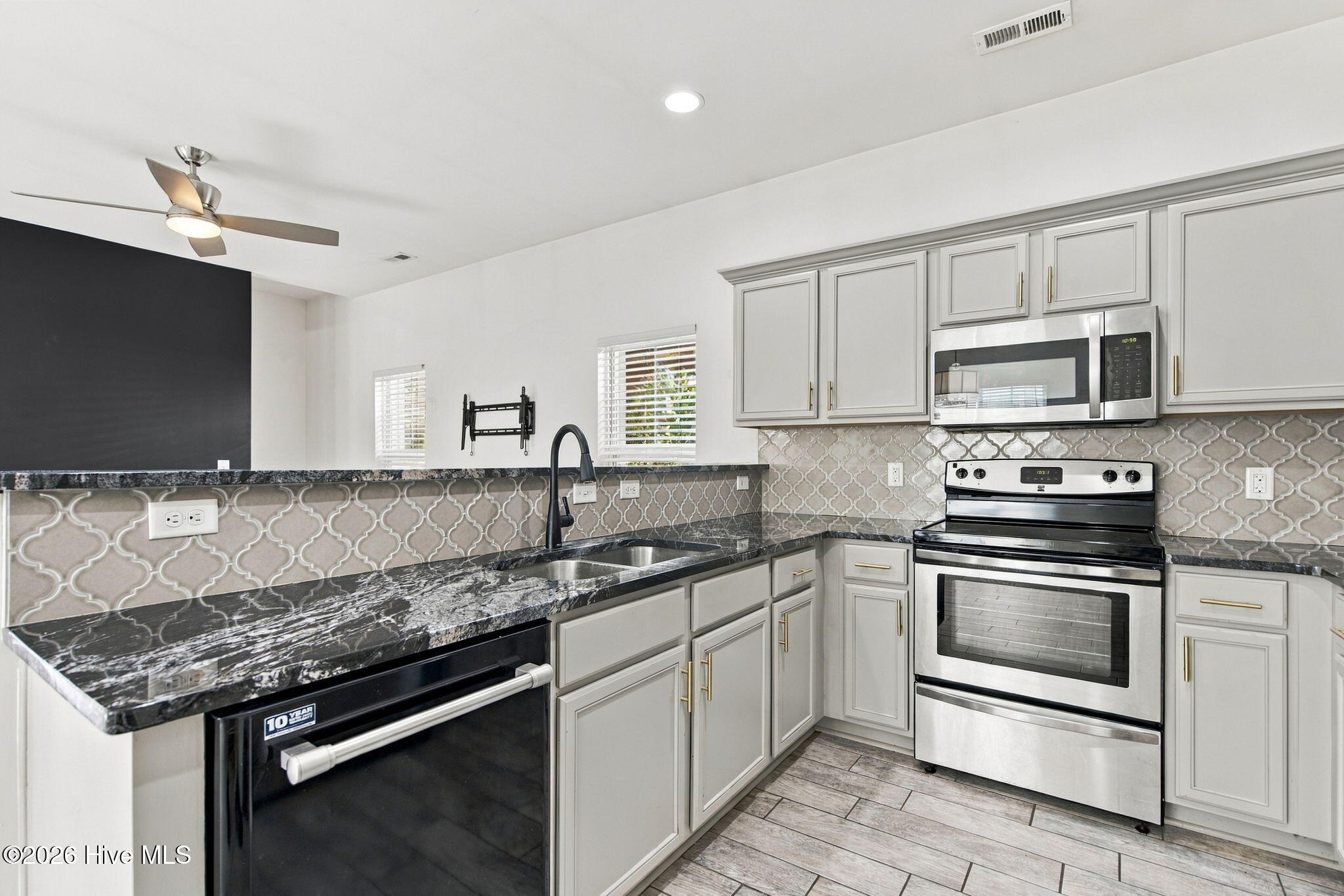 Kitchen with gray cabinets, granite counters, patterned backsplash, and stainless steel appliances.