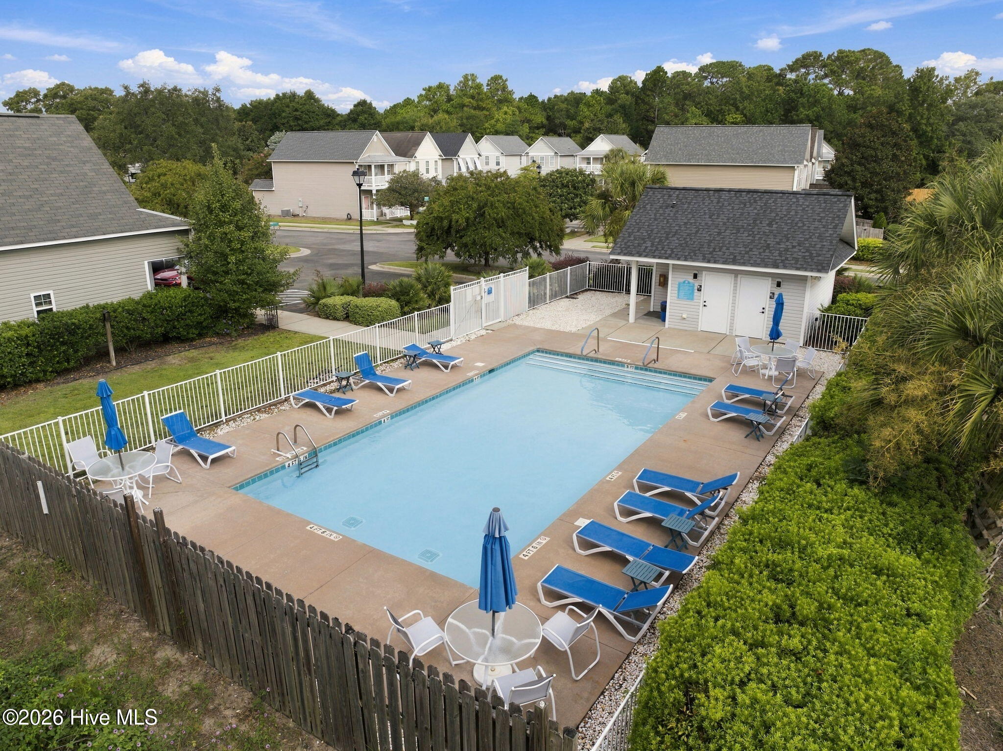 Aerial view of a fenced community pool with blue loungers and a small pool house.