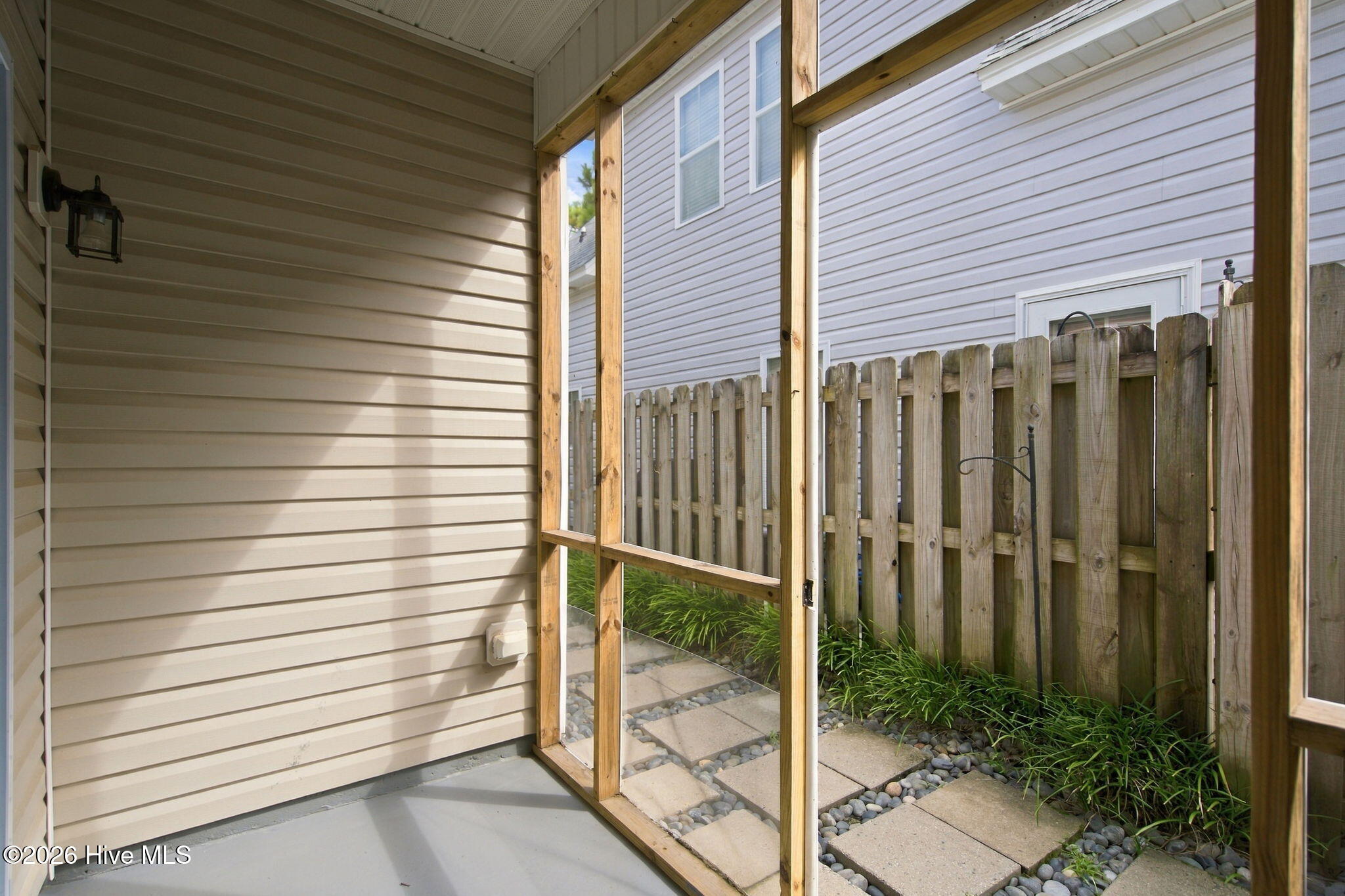 Screened porch overlooking a paver walkway and planted strip beside a tall wooden privacy fence.