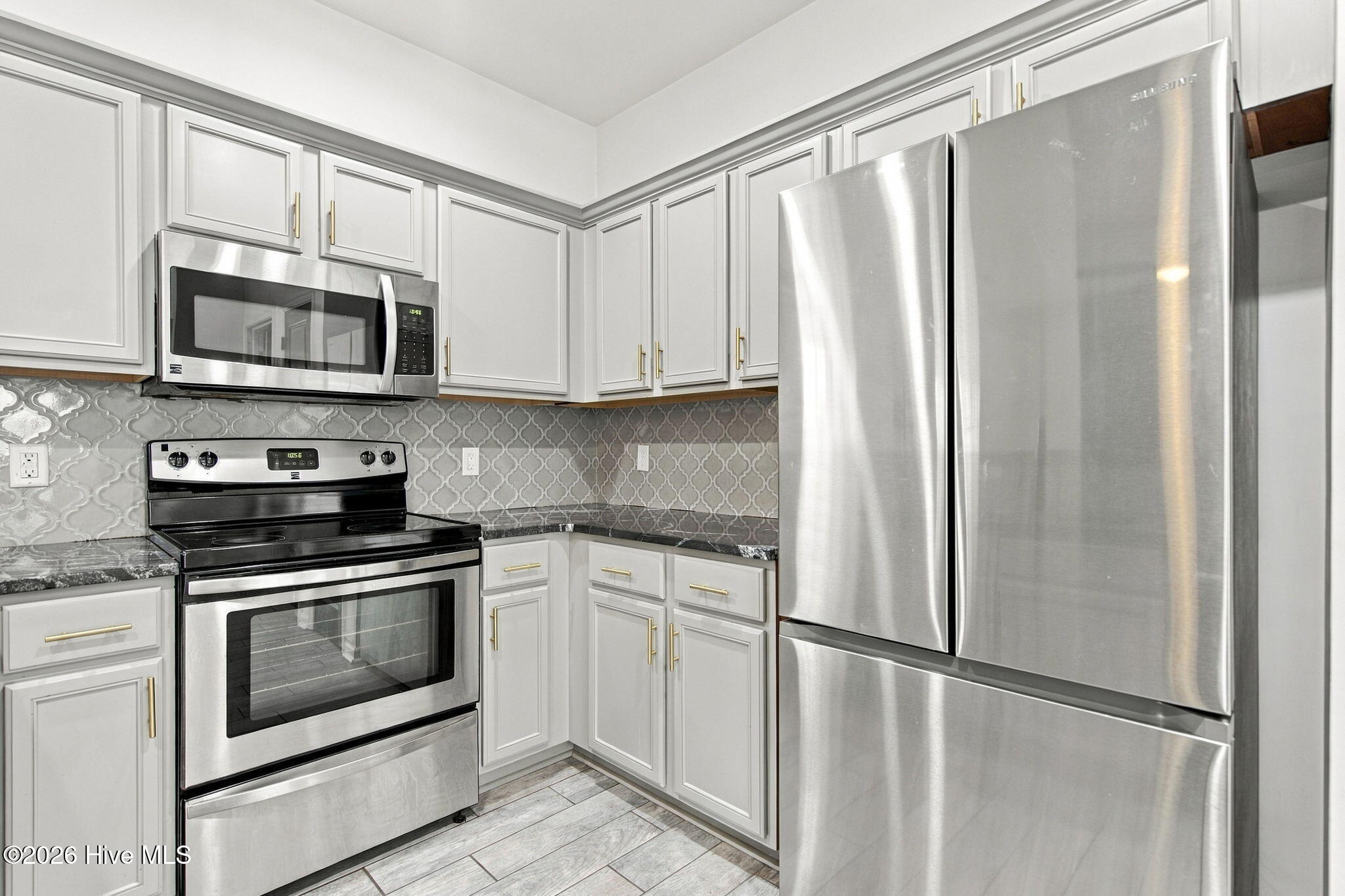 Kitchen with white cabinets, patterned gray backsplash, stainless steel appliances, and light tile flooring.