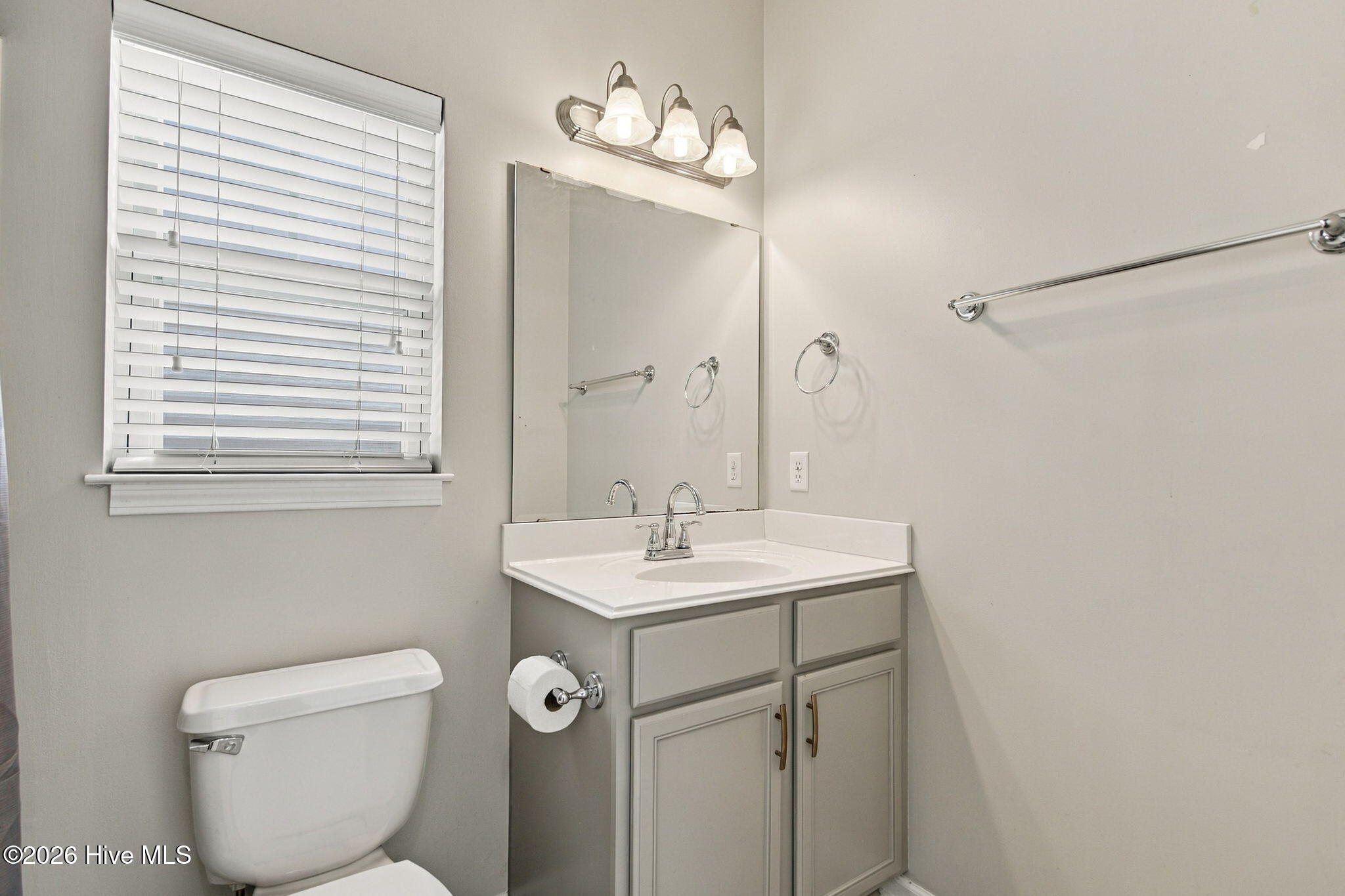 Bathroom vanity with a large mirror and window with white blinds.