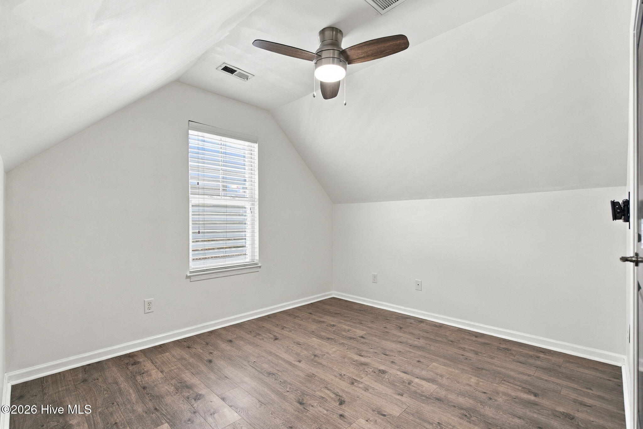 Empty upstairs room with a sloped ceiling, wood-look flooring, window blinds, and a ceiling fan.