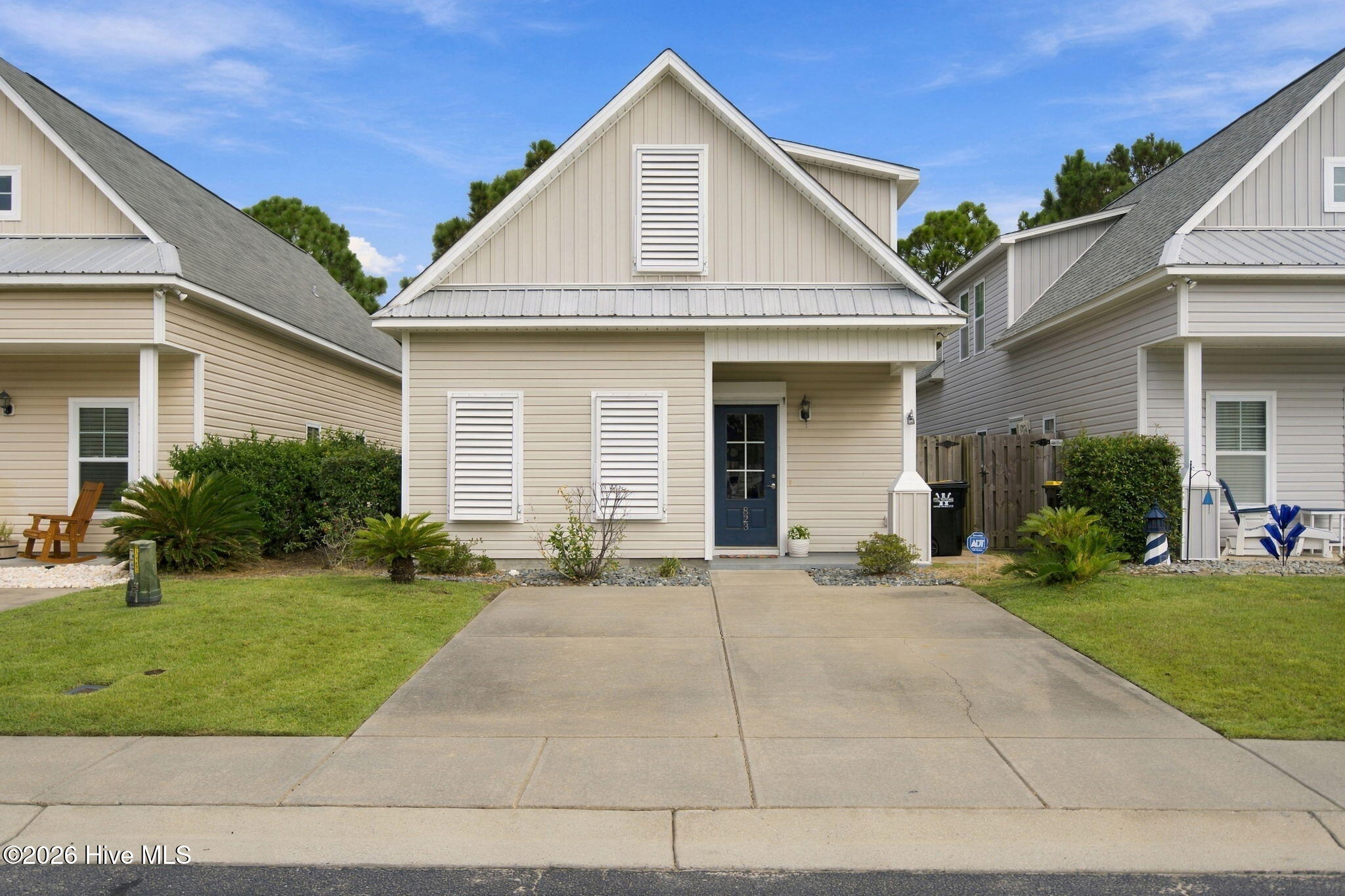 Beige gabled home with a dark blue front door, wide driveway, and landscaped lawn.