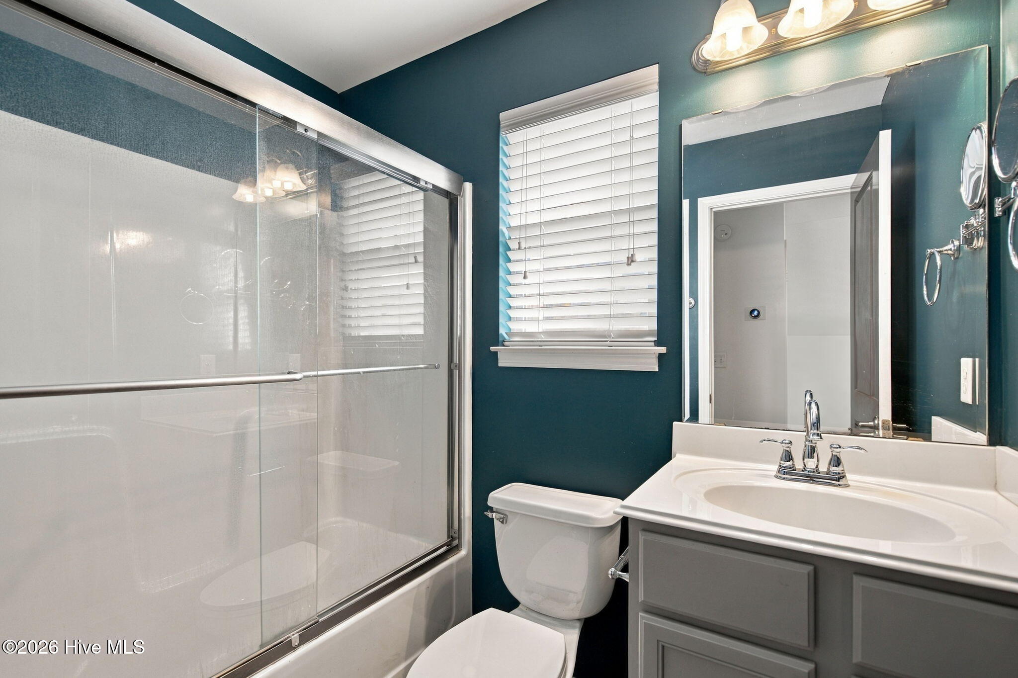 Bathroom with glass-enclosed tub and shower, gray vanity, and dark teal walls.