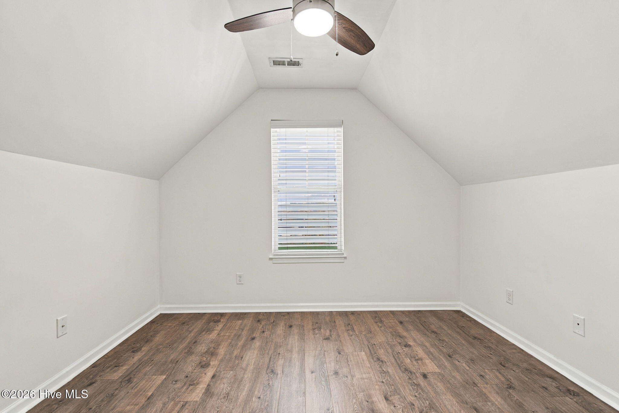 Empty vaulted room with wood-look flooring, a centered window, and a ceiling fan.
