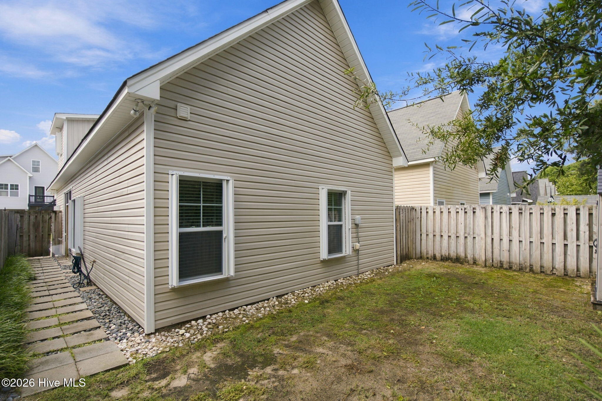 Beige-sided house beside a fenced yard, with a stone walkway along the side.