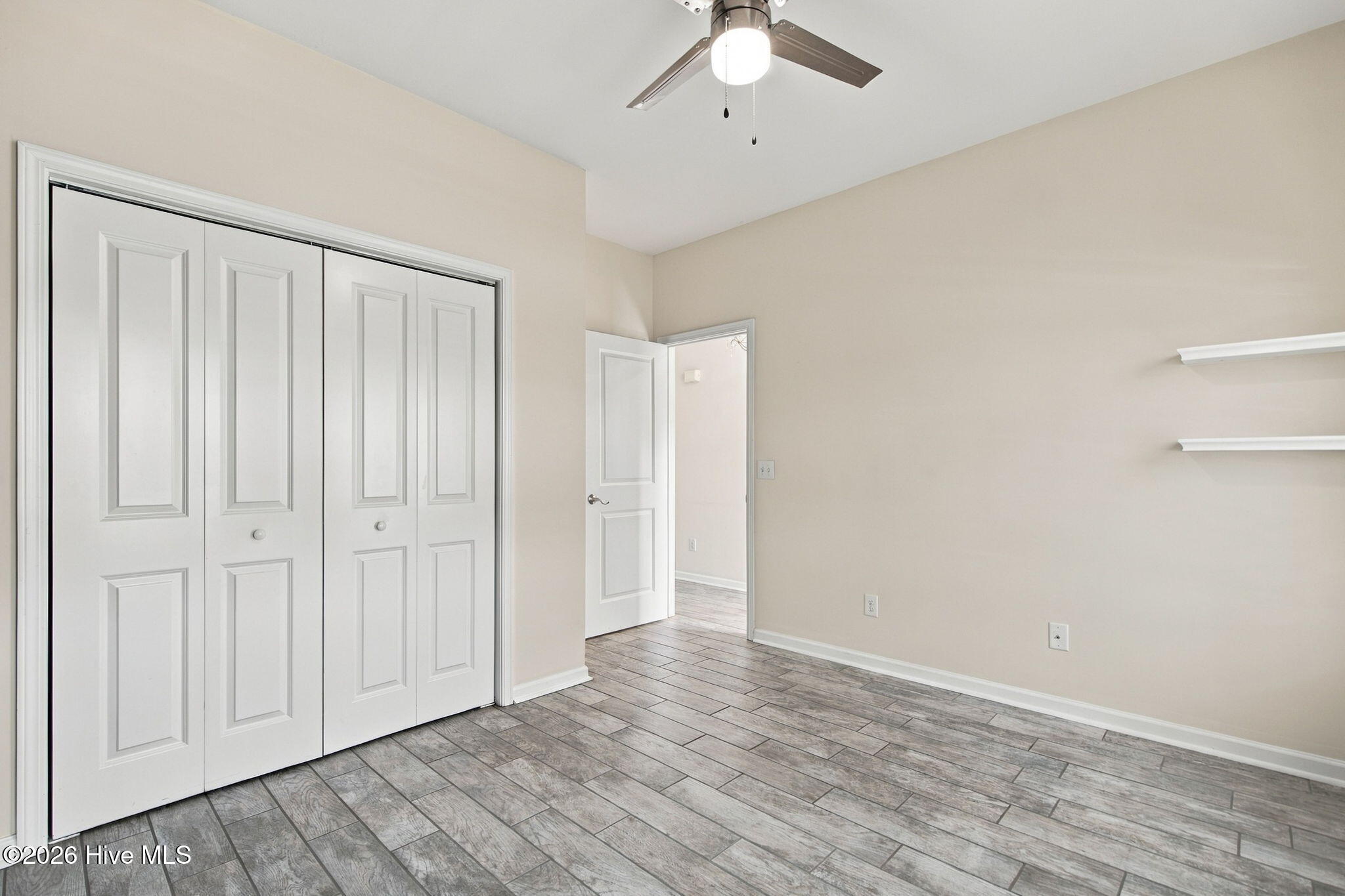 Empty bedroom with gray wood-look tile flooring, white closet doors, and a ceiling fan.