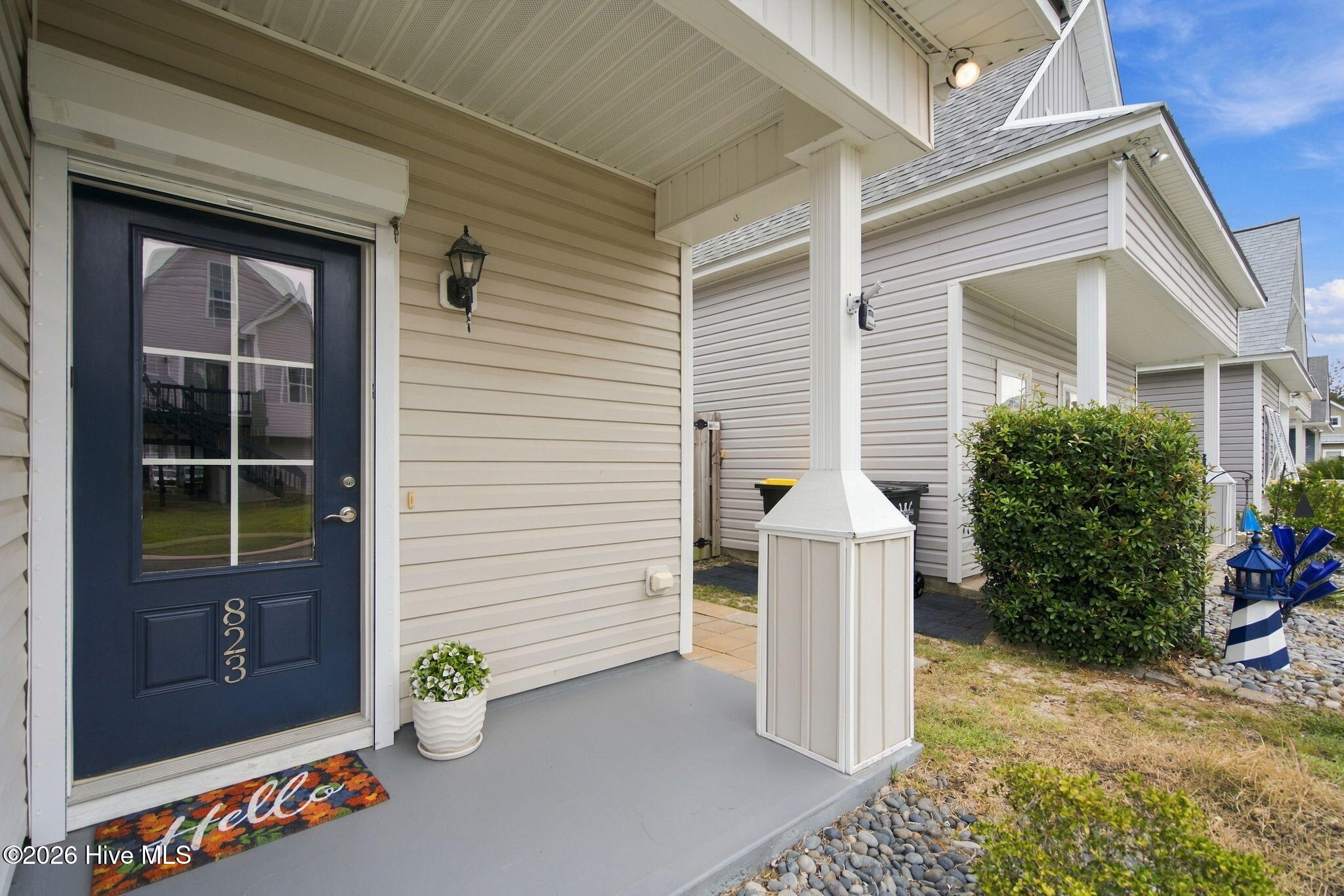 Covered porch with navy door marked 823, a potted plant, and a colorful welcome mat.