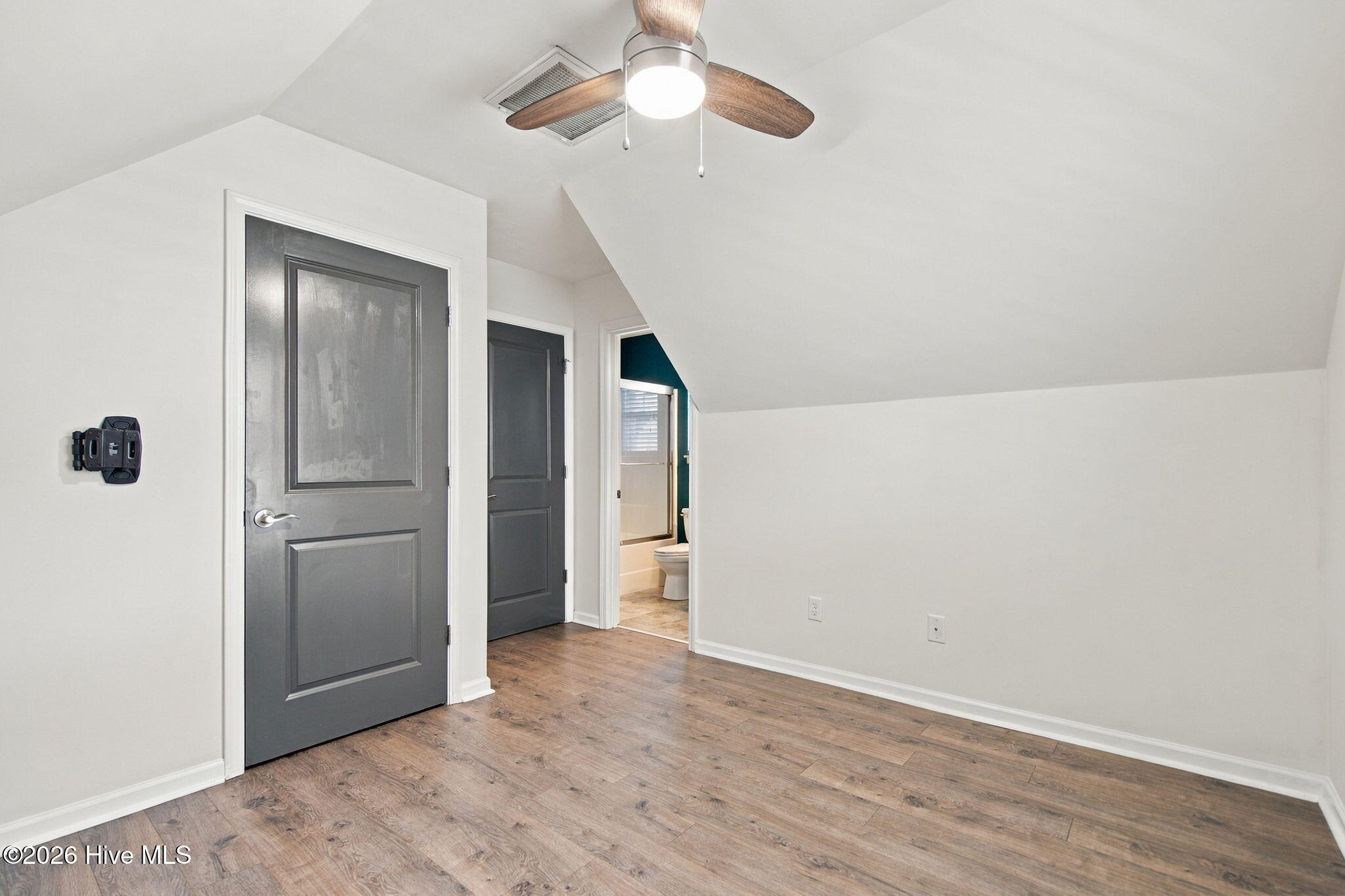Empty bedroom with wood-look flooring, a ceiling fan, and an open doorway to the bathroom.