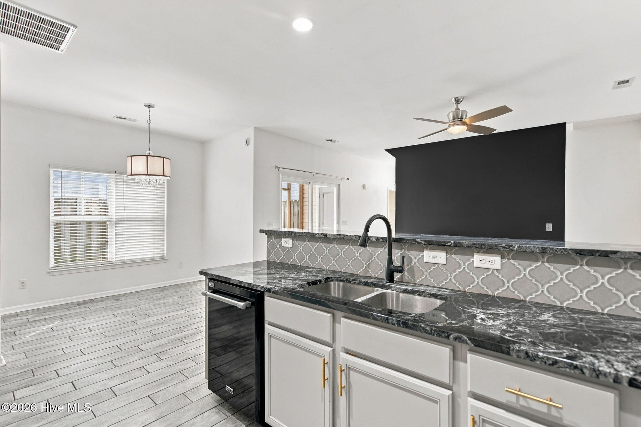 Vacant kitchen with gray cabinets, dark counters, patterned backsplash, and an adjoining dining area.