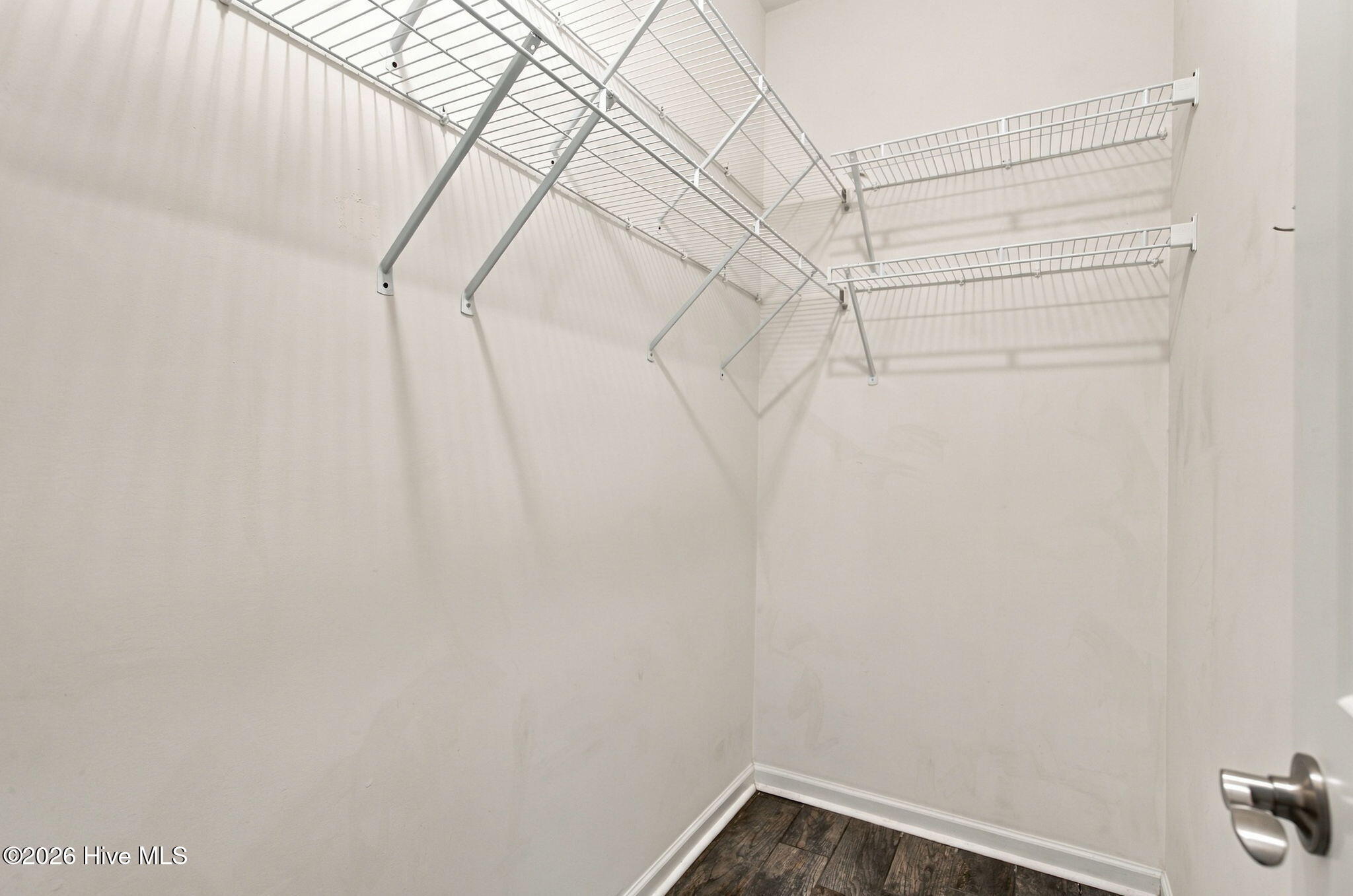 Empty walk-in closet with white wire shelving and dark wood-look flooring.