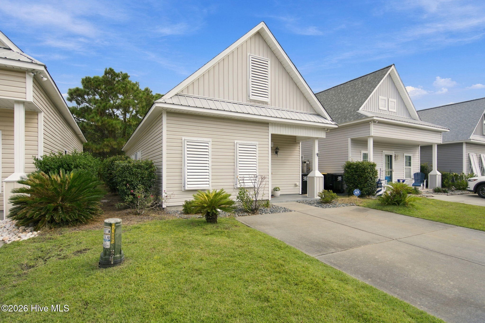 Beige gable-roofed home with white shutters, a covered entry, and landscaped front lawn.