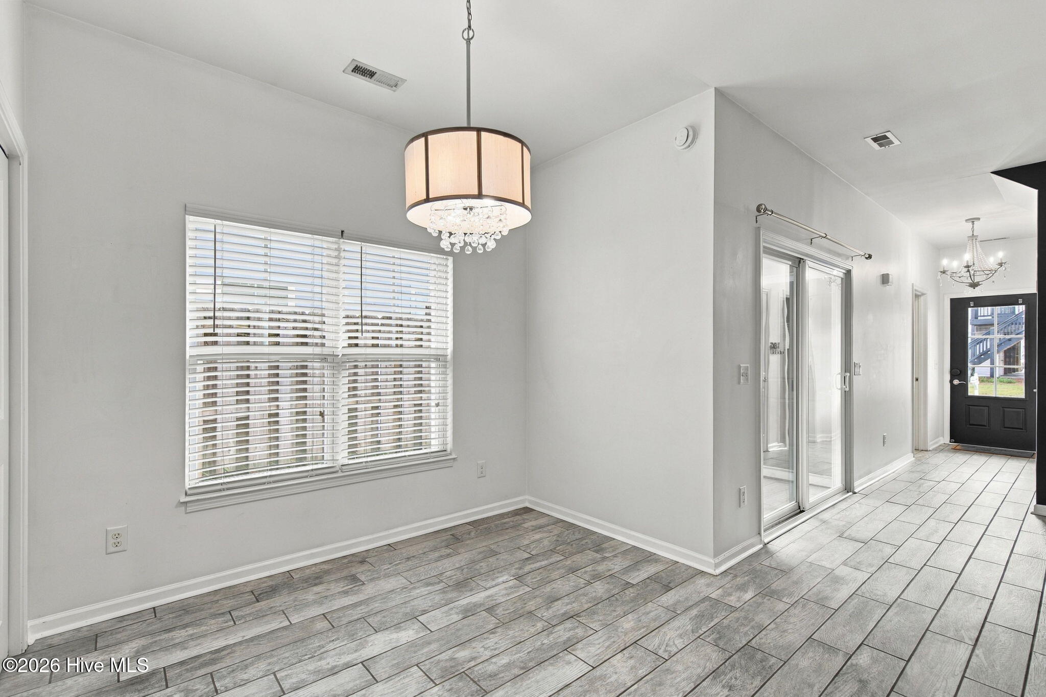 Vacant dining area with gray tile floors, a wide blinded window, and a crystal-accented drum pendant light.