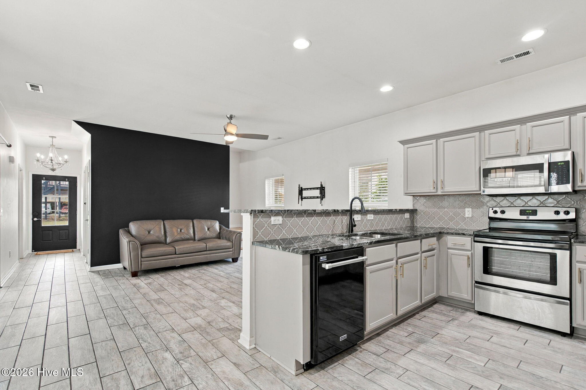 Open-plan kitchen and living area with gray cabinetry, patterned backsplash, and a sofa against a charcoal wall.