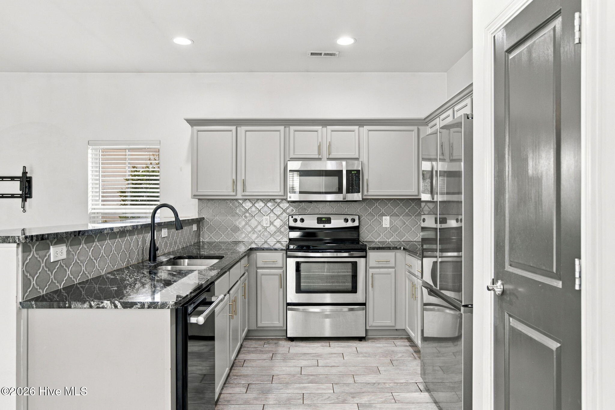 Kitchen with gray cabinetry, patterned tile backsplash, dark countertops, and stainless steel appliances.