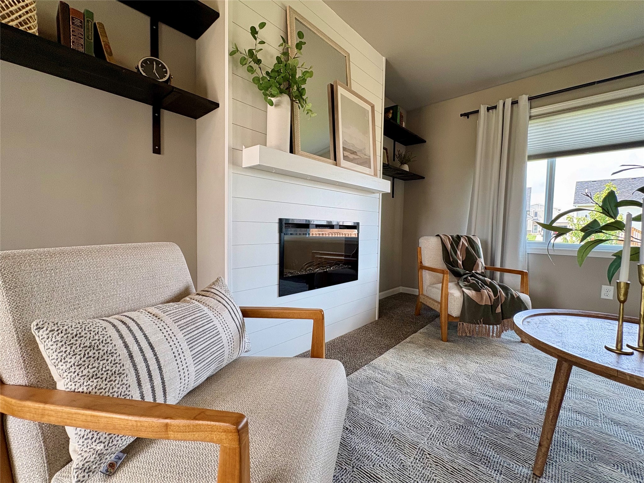 Living room with a white shiplap fireplace, neutral chairs, and a large curtained window.