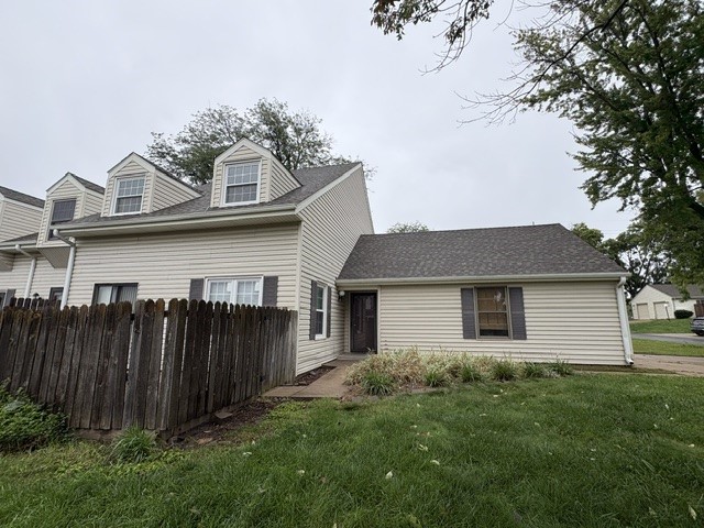 Beige suburban home with dormer windows, a weathered wooden fence, and a grassy yard.