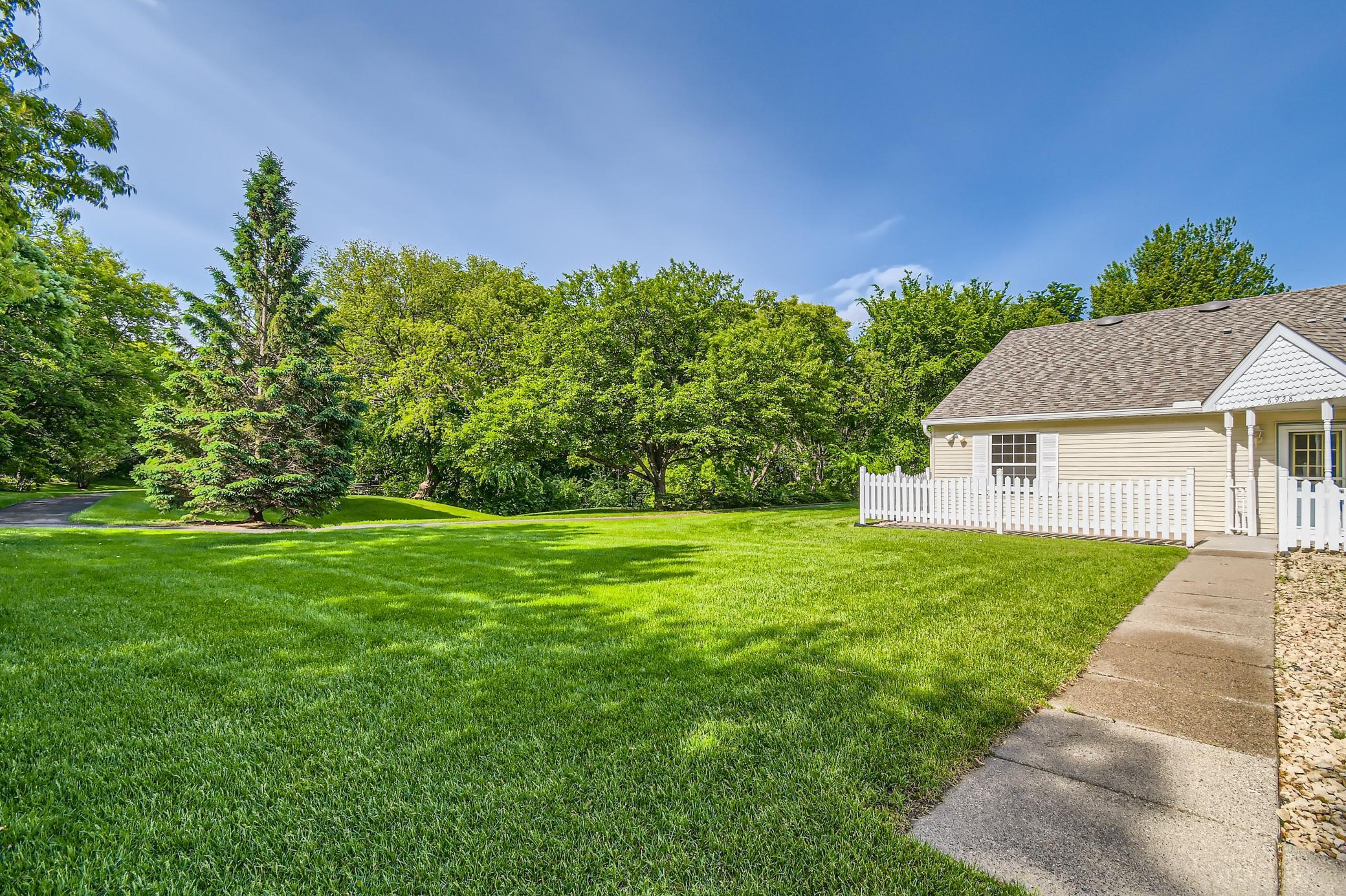 Light-colored house beside a broad green lawn, white picket fence, and mature trees.