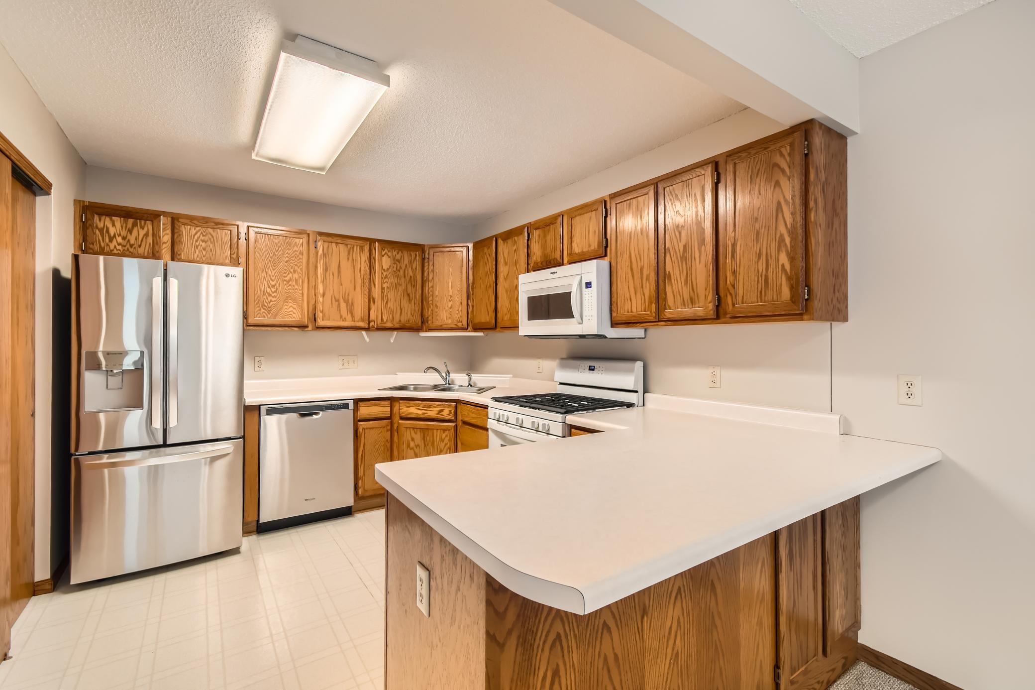 Kitchen with oak cabinets, a large white-countertop peninsula, and stainless steel appliances.